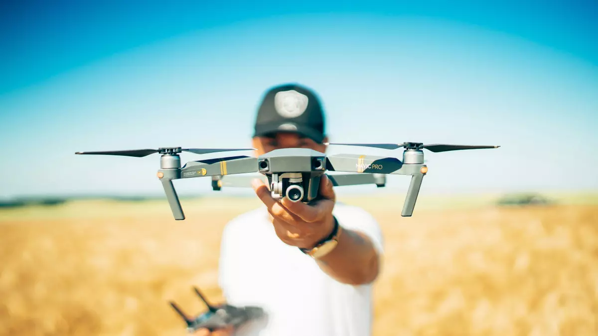 A drone flying over a field of tall grass. The sky is blue and the grass is a light yellow.