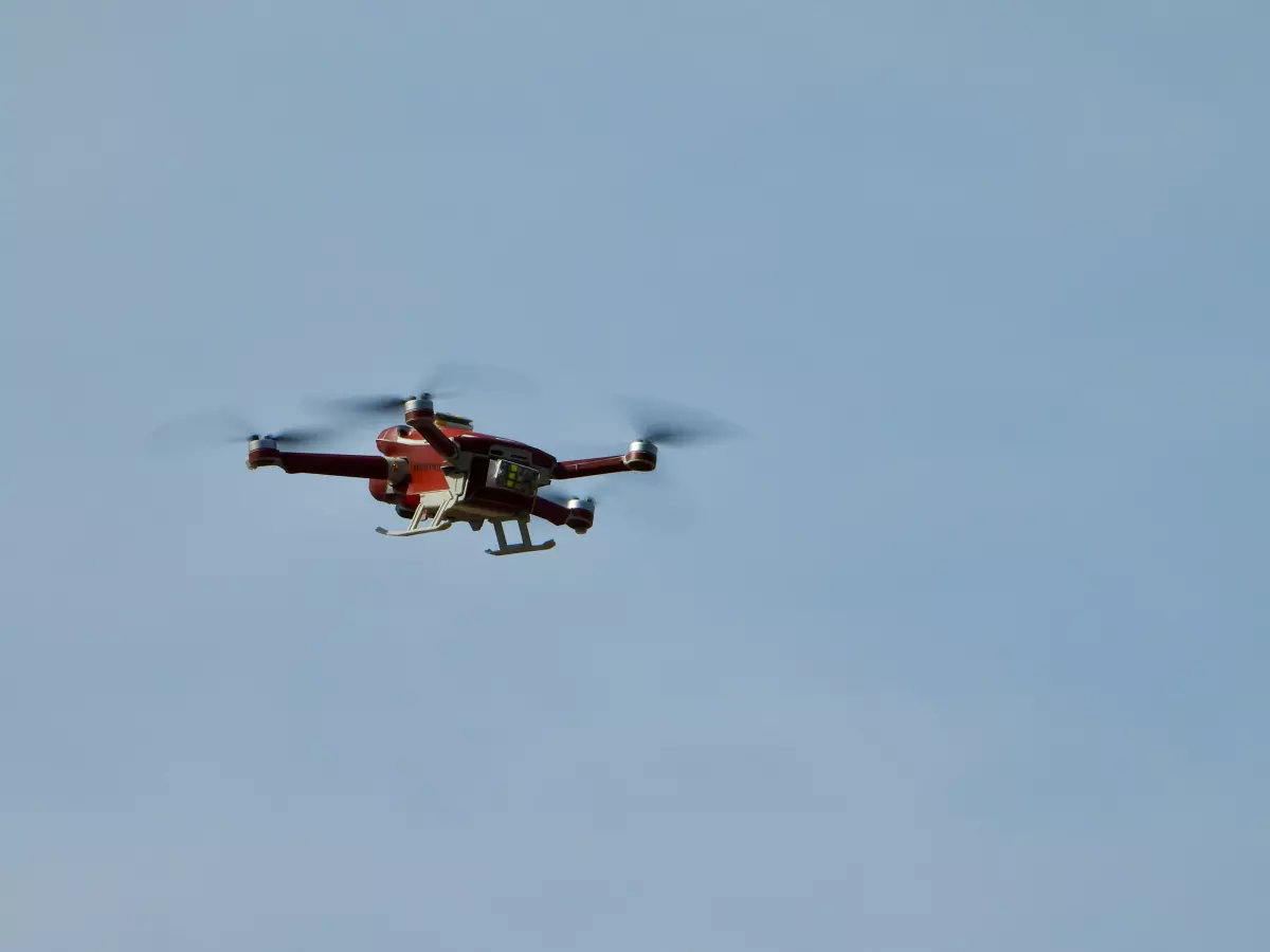 A red drone with four propellers flying in a clear blue sky.