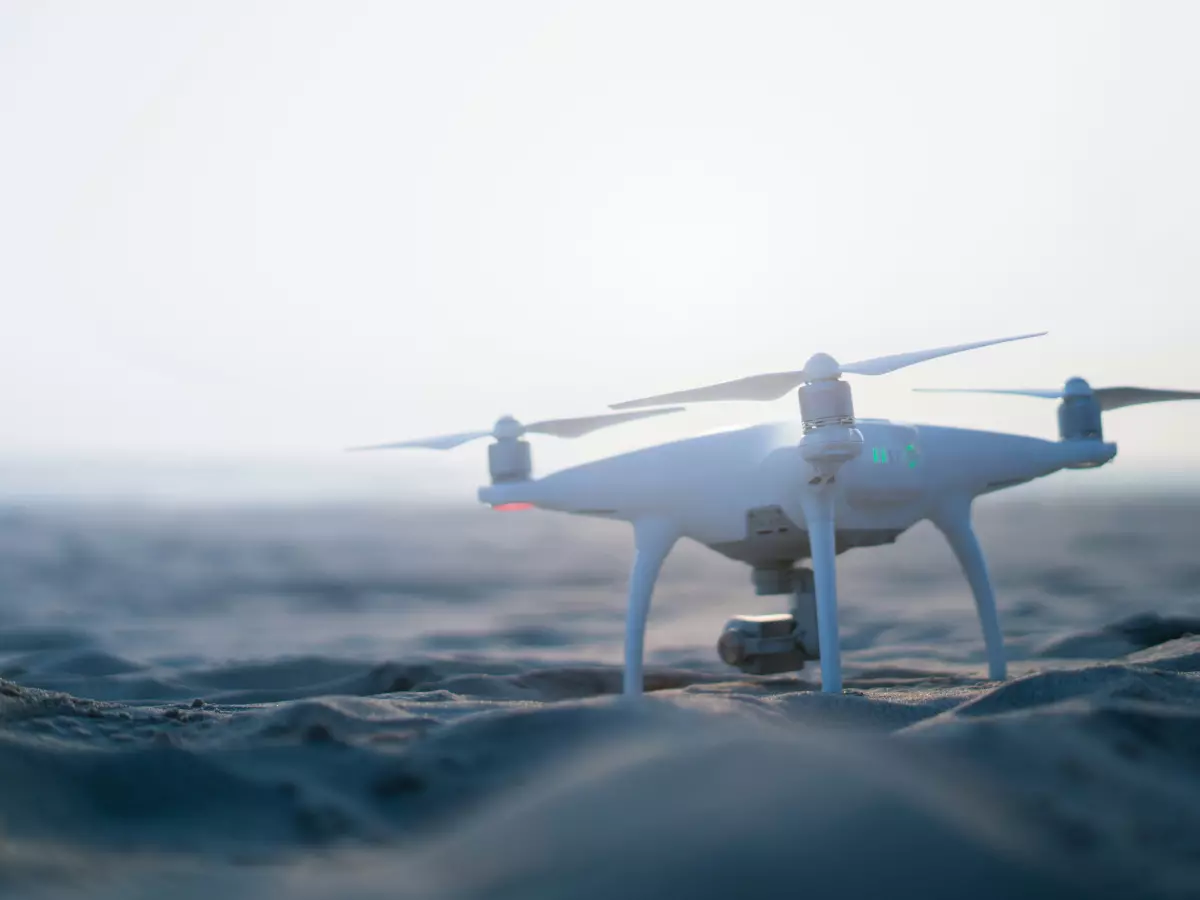 A white drone sitting on a sandy beach, with a blurred out background.