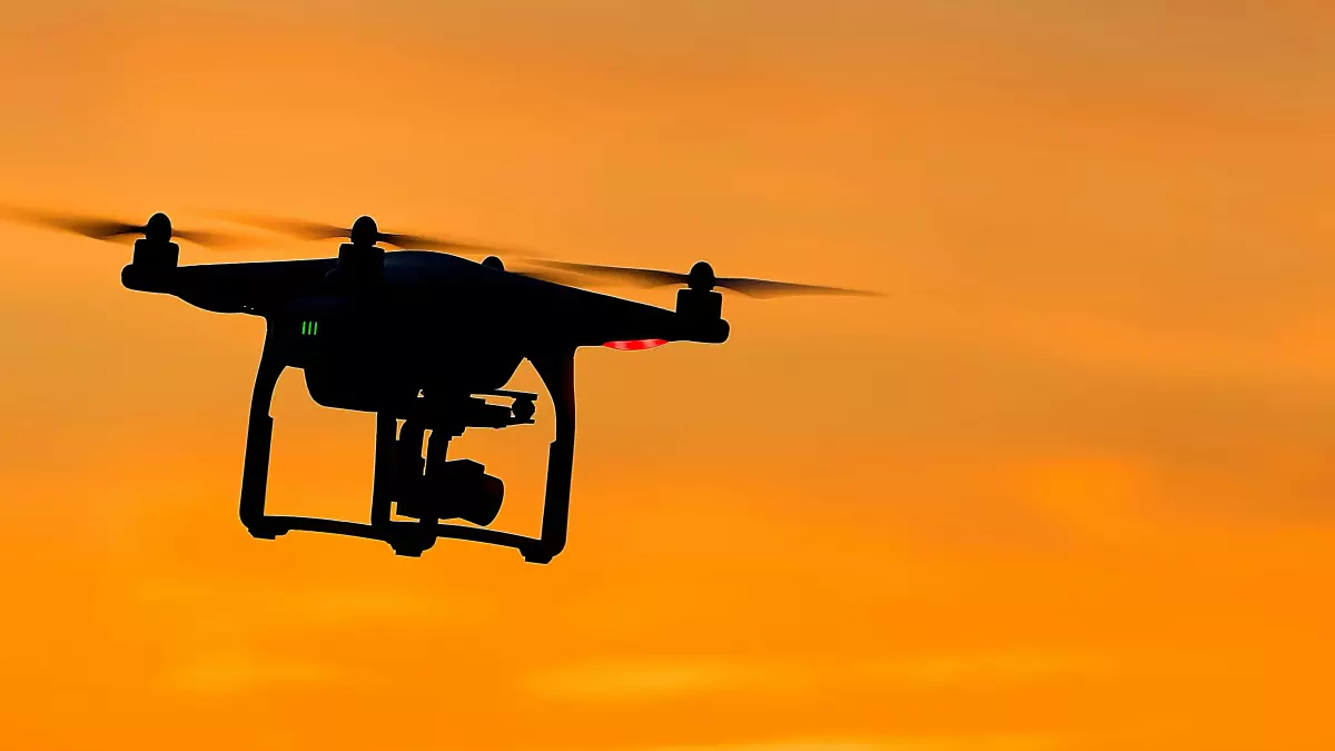 A drone flying against a vibrant orange sunset, with a slight blur to the background and a focused shot on the drone.