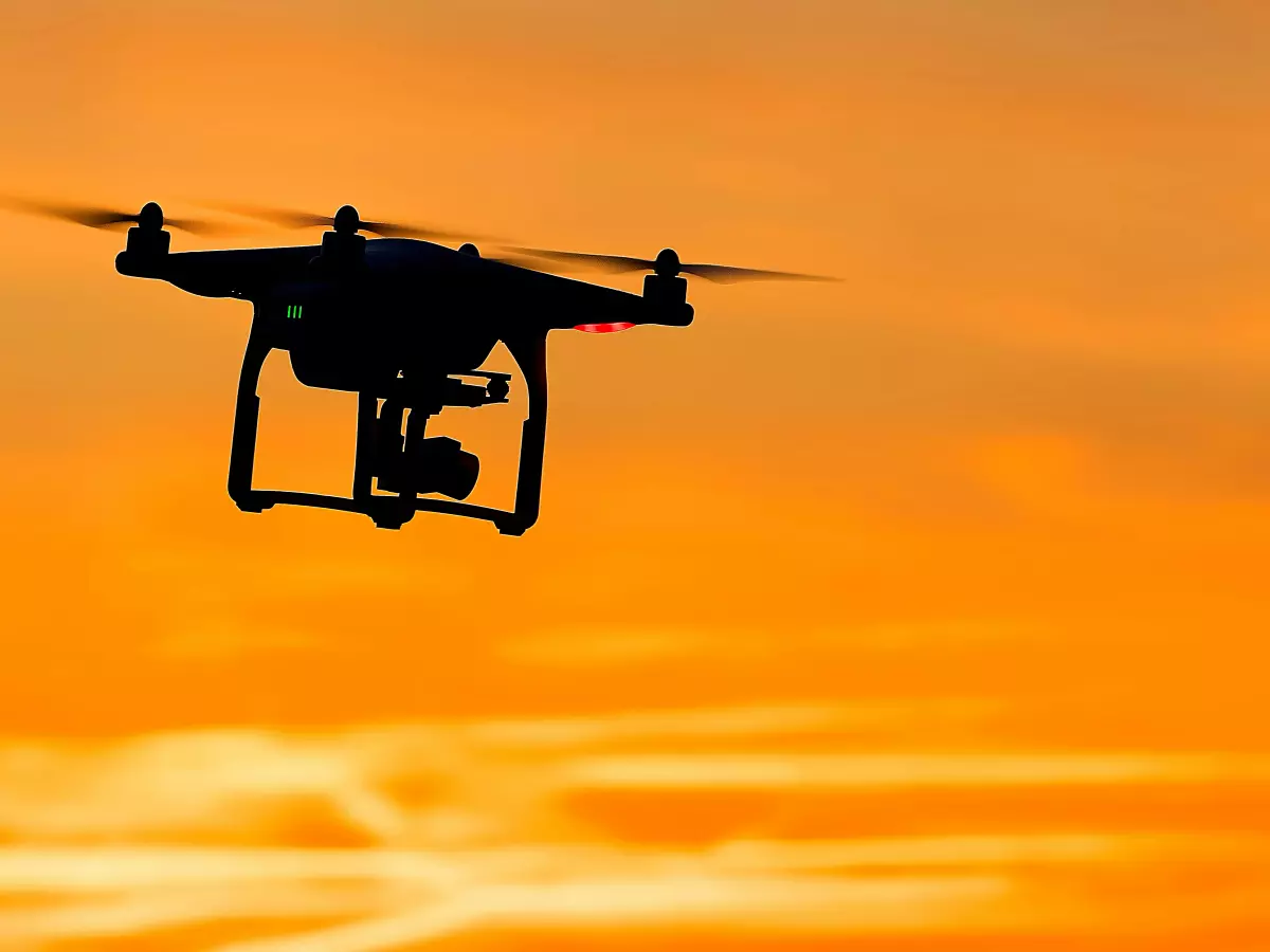 A drone flying against a vibrant orange sunset, with a slight blur to the background and a focused shot on the drone.