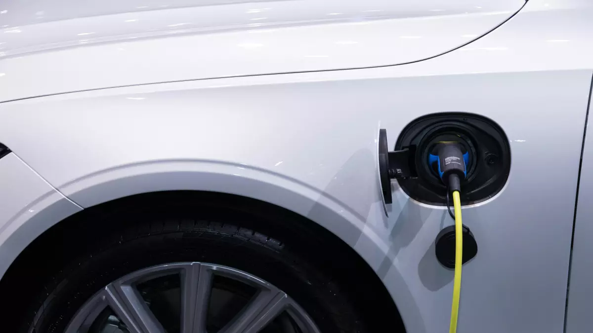 A close-up of a white electric vehicle being charged. The charging cable is plugged into the car