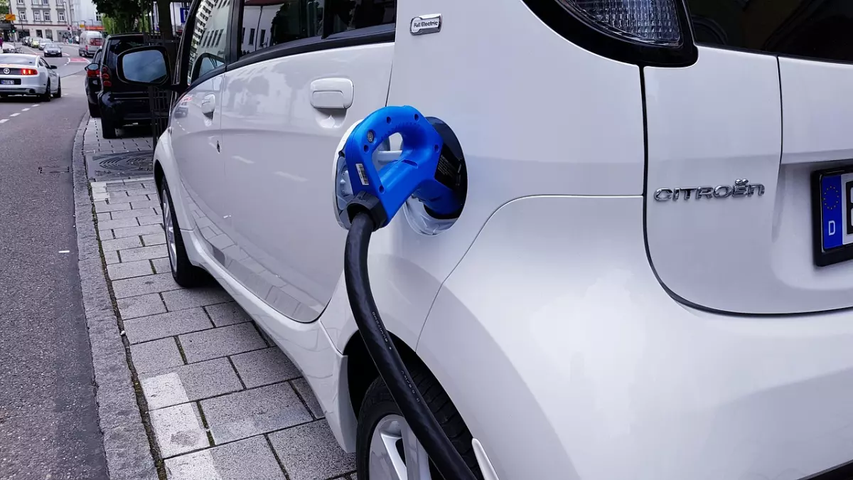 A white Citroen electric car being charged with a blue charging cable.