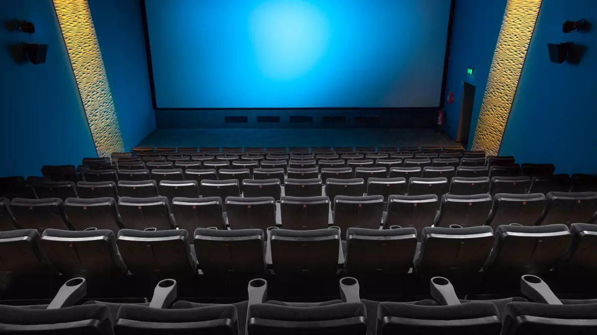 A wide shot of a cinema theatre with rows of empty seats and a large screen with blue lighting.