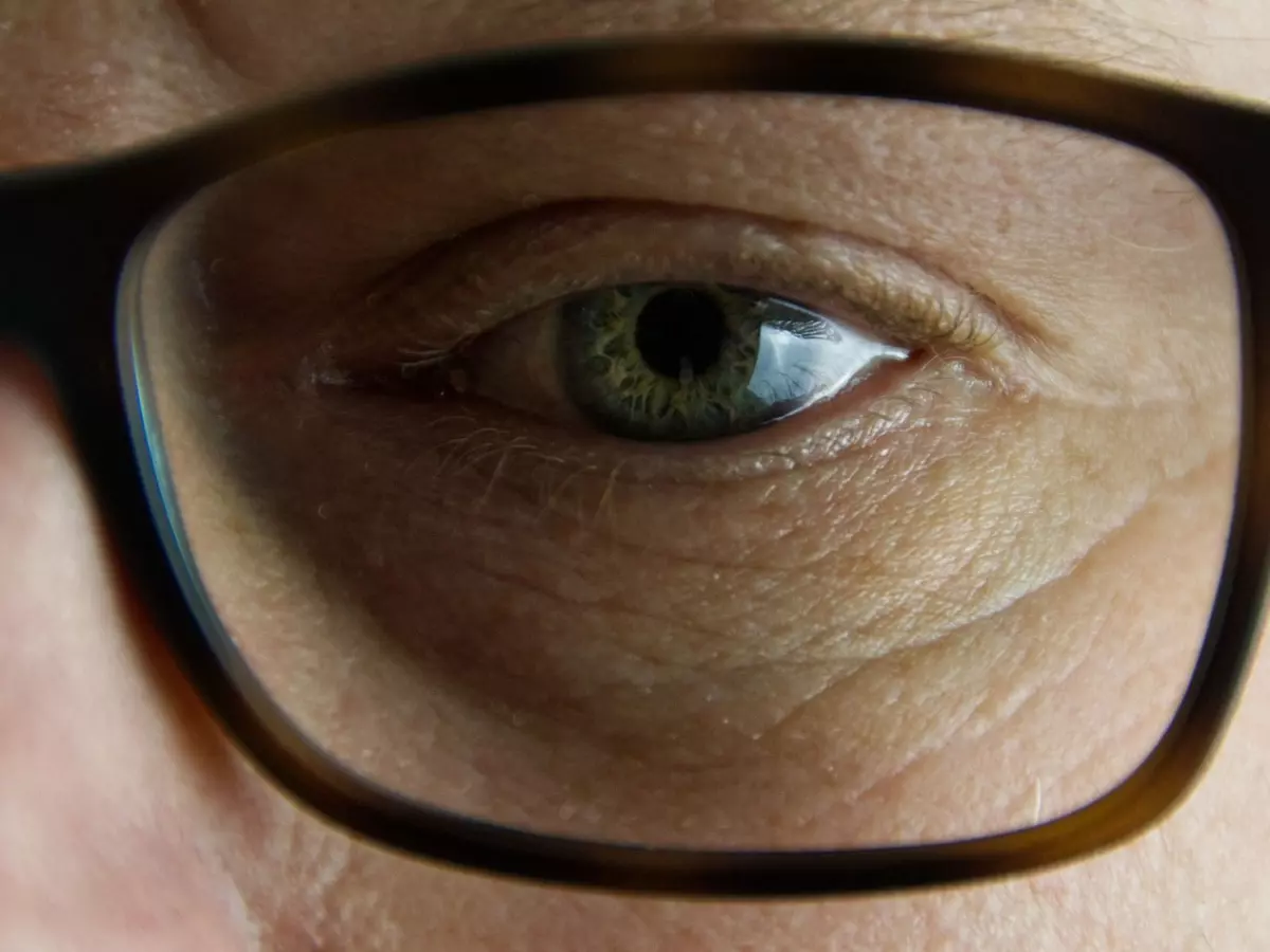 A close-up shot of a person's eye looking at the camera. The person is wearing tortoiseshell glasses.