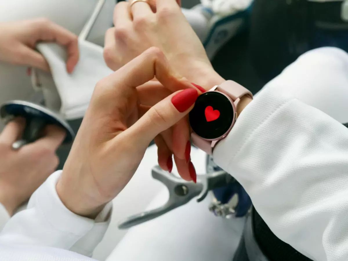 Close-up shot of a woman's wrist displaying a smartwatch with a prominent red heart rate monitor on the screen.