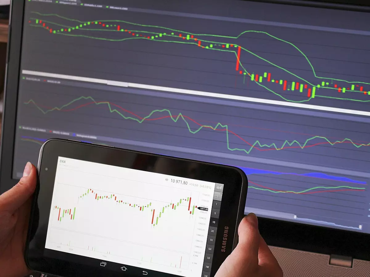 A close-up of a laptop screen showing multiple crypto charts, with a tablet device in the foreground displaying a similar chart.