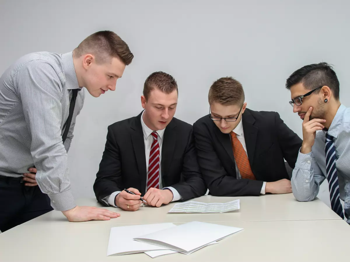 Four business men in suits seated at a table discussing something.