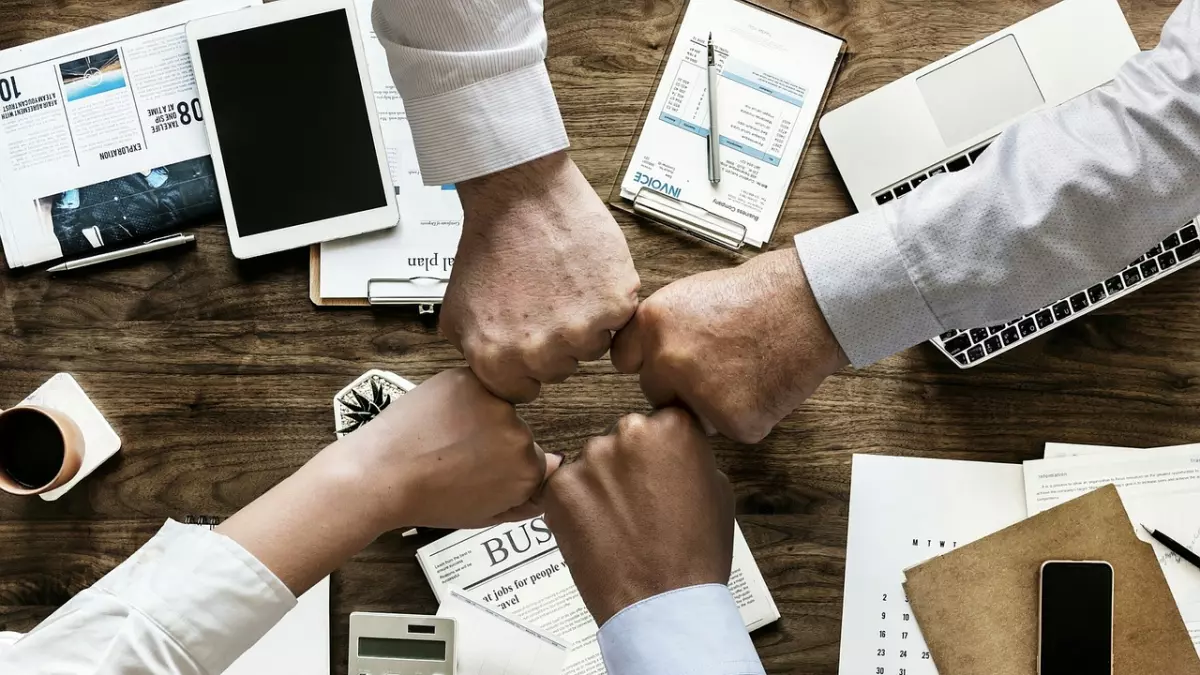 Four hands clasped together in the center of a desk, surrounded by office supplies, symbolizing teamwork and collaboration.