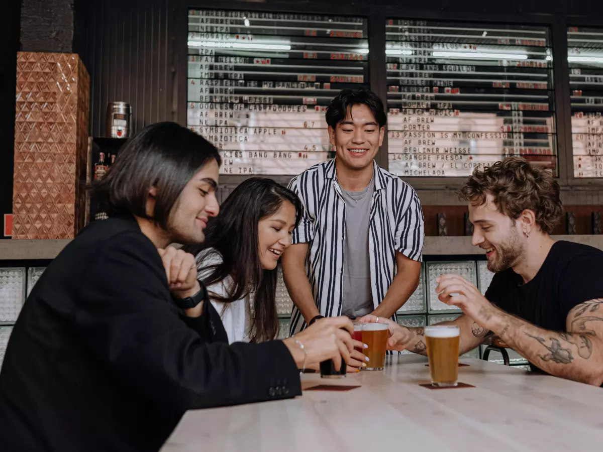 Four friends laughing and having drinks at a bar.