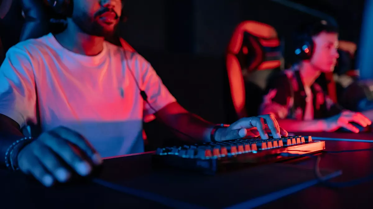 A person is seated in a dark room, wearing headphones and concentrating on a computer keyboard, the screen is illuminated with a bright, colorful light.