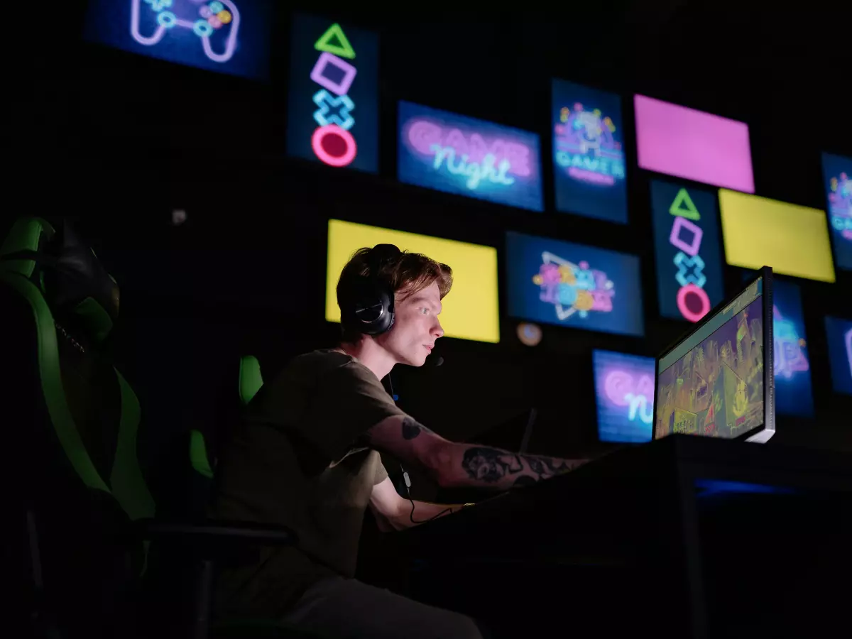 A gamer playing a video game in a dark room. The player is wearing a headset and has a glowing screen in front of them.