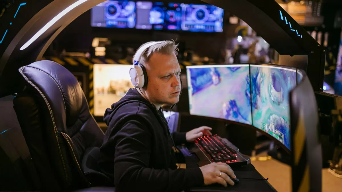 A gamer in a dark room, wearing headphones and using a keyboard, playing a game on a computer screen. The gamer is wearing a suit, and the room is set up for gaming.