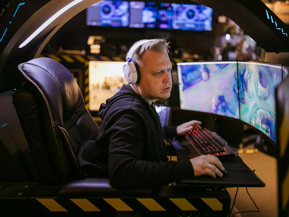 A gamer in a dark room, wearing headphones and using a keyboard, playing a game on a computer screen. The gamer is wearing a suit, and the room is set up for gaming.