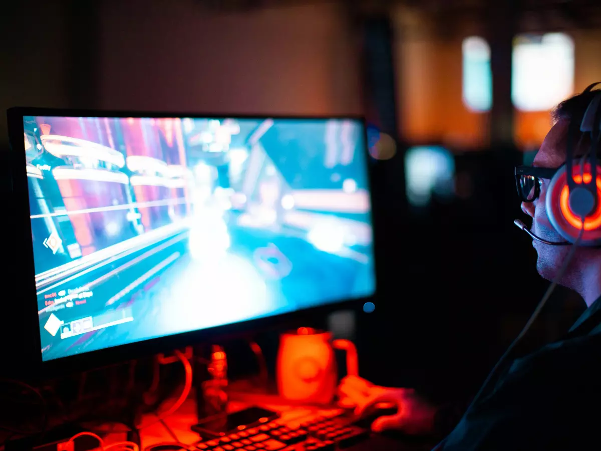 A gamer sitting in a chair wearing headphones and looking at a monitor, playing a video game.