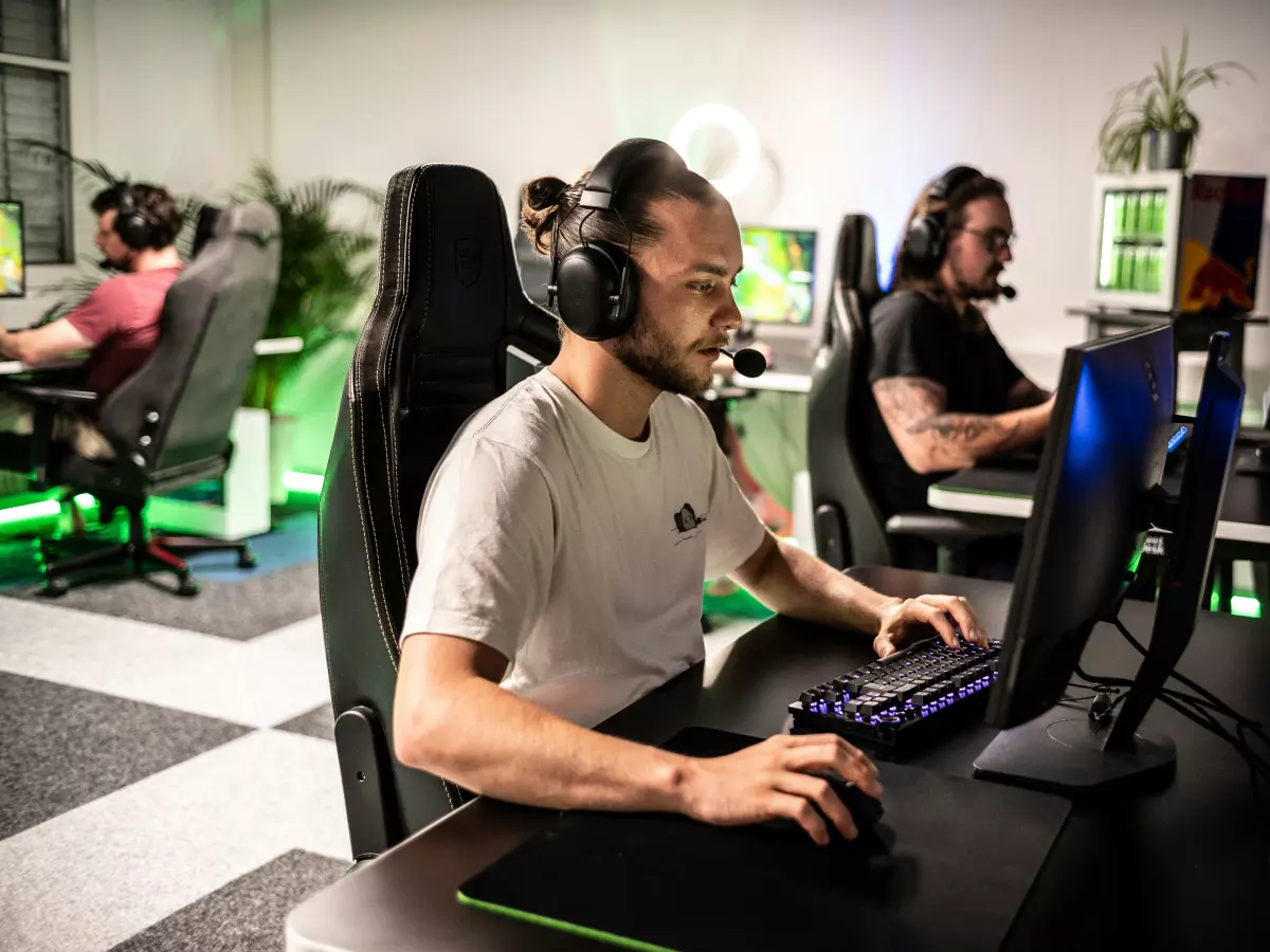 Two men in a gaming room, wearing headsets and playing on computers. 