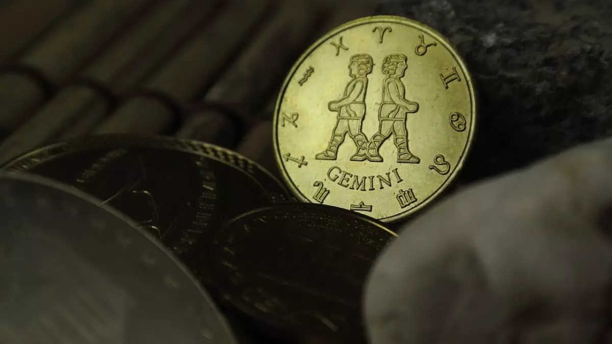 A close-up shot of a gold coin with the Gemini zodiac symbol. The coin is resting on a wooden surface and is surrounded by other coins.