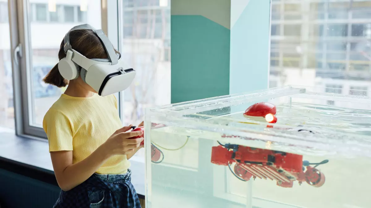 A person wearing a VR headset looks into a tank of water where a red robot is submerged. The robot is partially visible through the water.