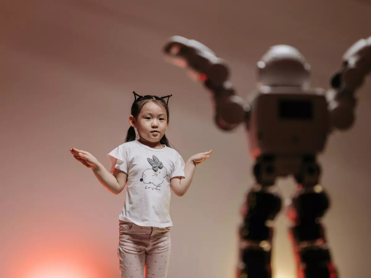 A humanoid robot stands in the background, while a young girl dances in the foreground.