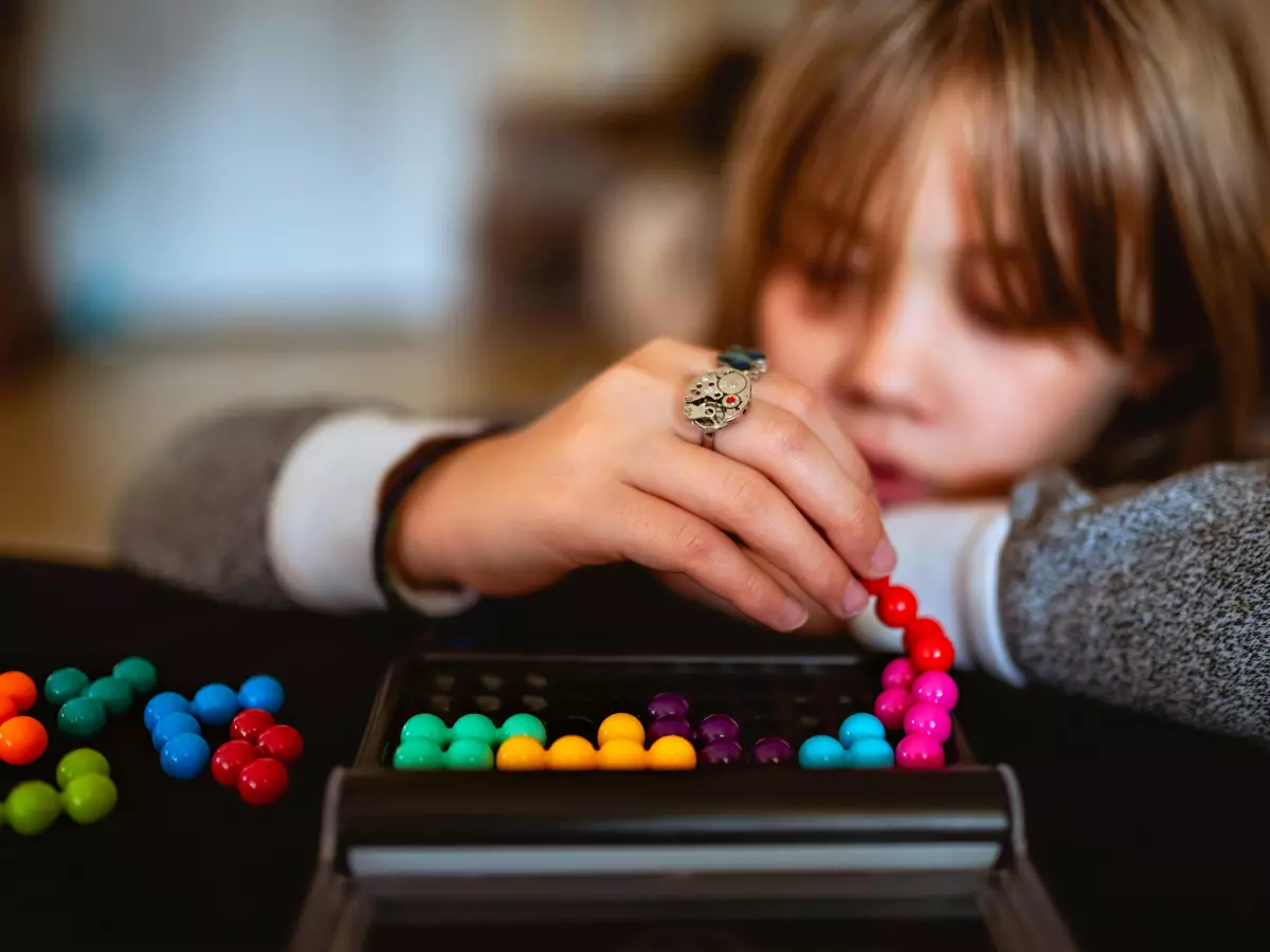 A young girl is playing with a NYT Strands puzzle, focusing intently on the colorful beads. She is leaning her head on her hand, suggesting a moment of concentration and strategy.