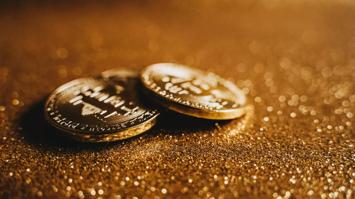 A close-up shot of two gold-colored cryptocurrency coins lying on a shiny gold surface.