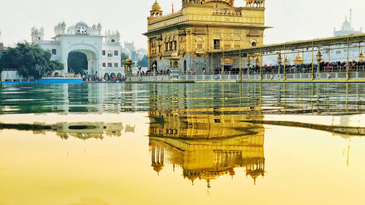 The Golden Temple in Amritsar, India, is reflected in a still pool of water. The temple is a beautiful golden structure, and the reflection creates a sense of depth and mystery.