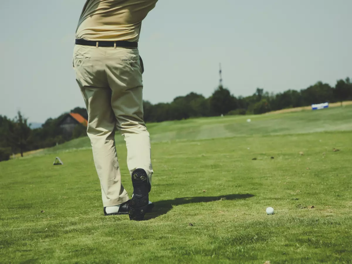 A golfer swings his club, the ball is in the foreground.