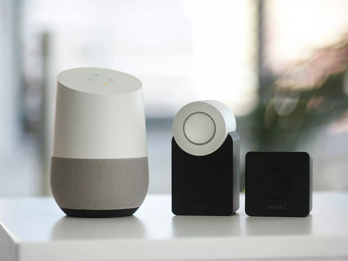 A Google Home smart speaker and two Muze devices on a white surface, with a blurred background.