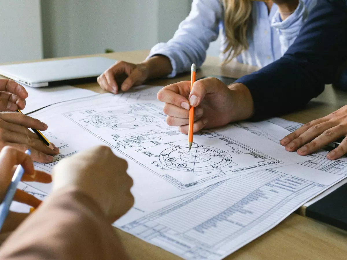 A group of people are sitting around a table, looking at a document and writing with pens.