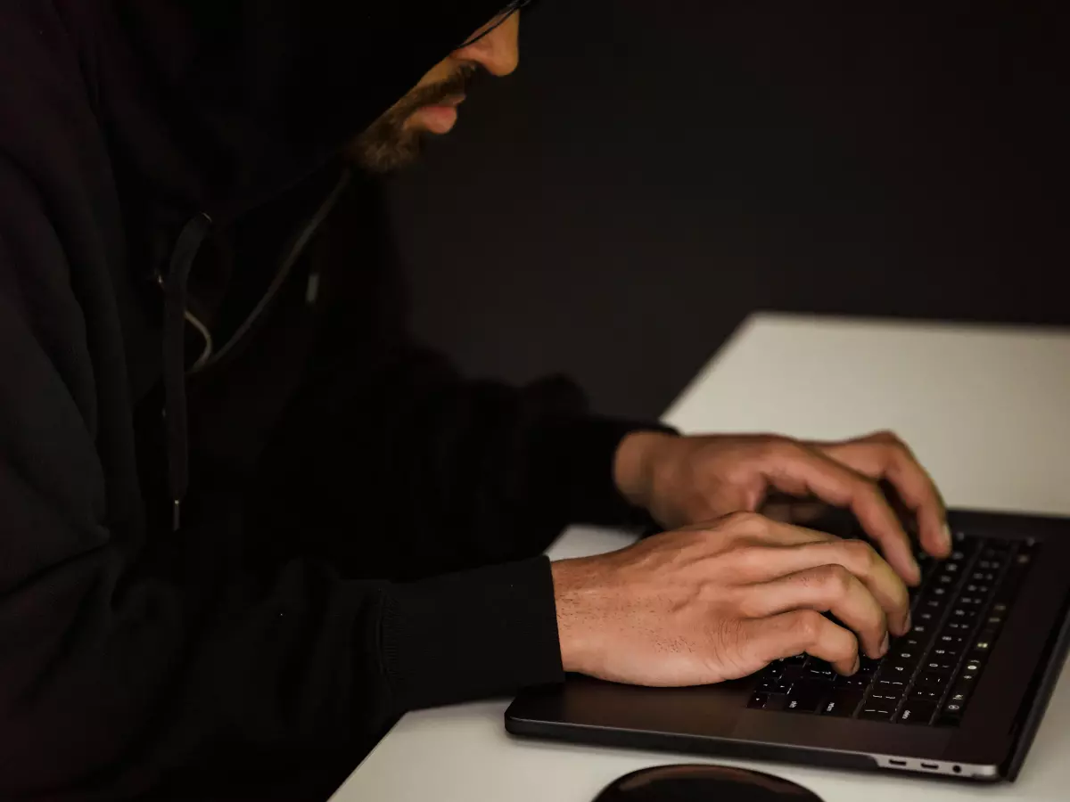 A person with their face hidden by a hood, typing on a laptop computer.