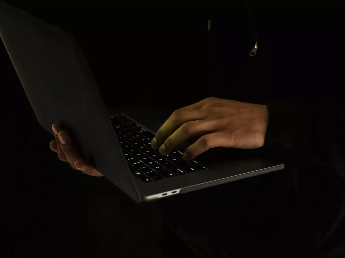 A person's hands typing on a laptop keyboard, with the rest of their body and face obscured by shadow.