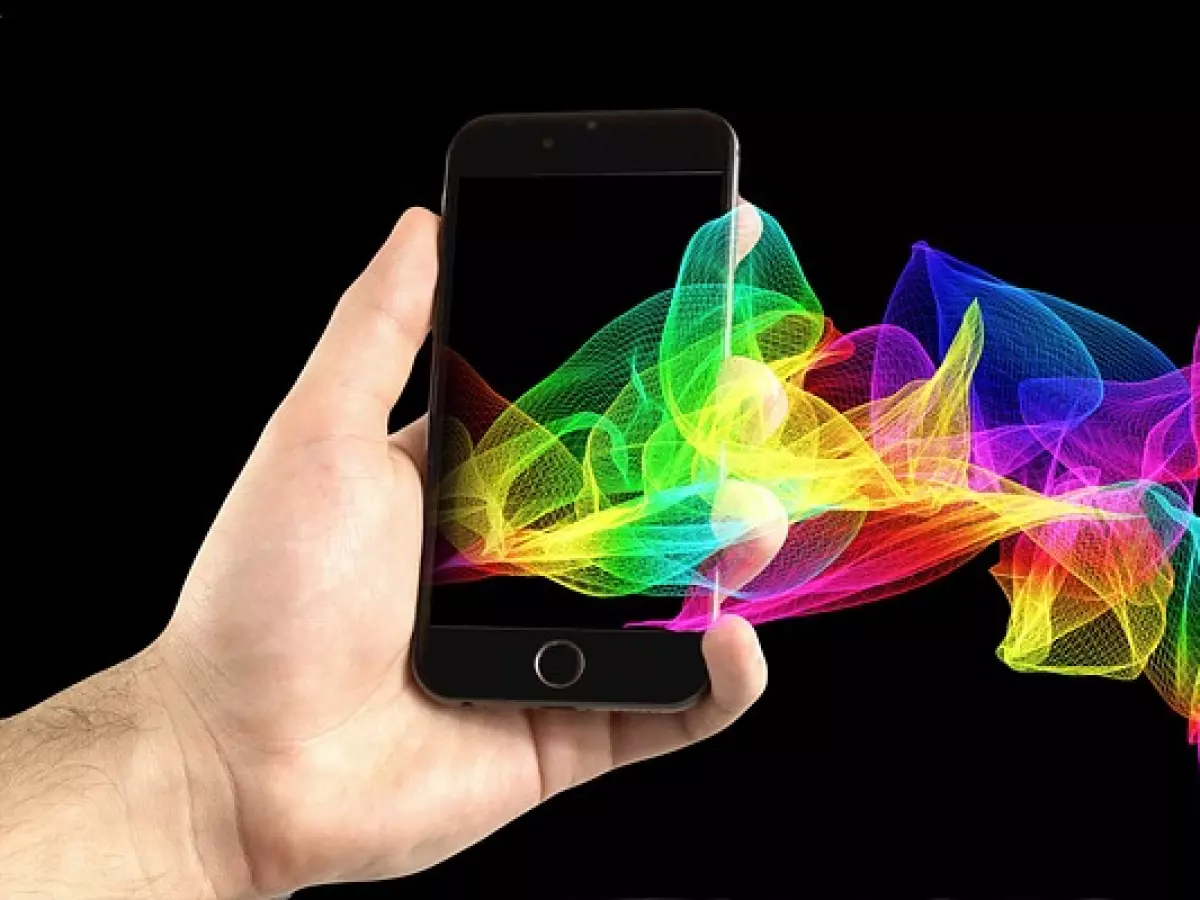 A hand holds a black smartphone with a thin bezel.  A colorful, abstract, wavy background of light, is behind the phone.