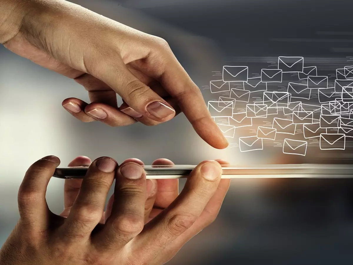 A person's hand is holding a smartphone and a few email icons are flying around it.