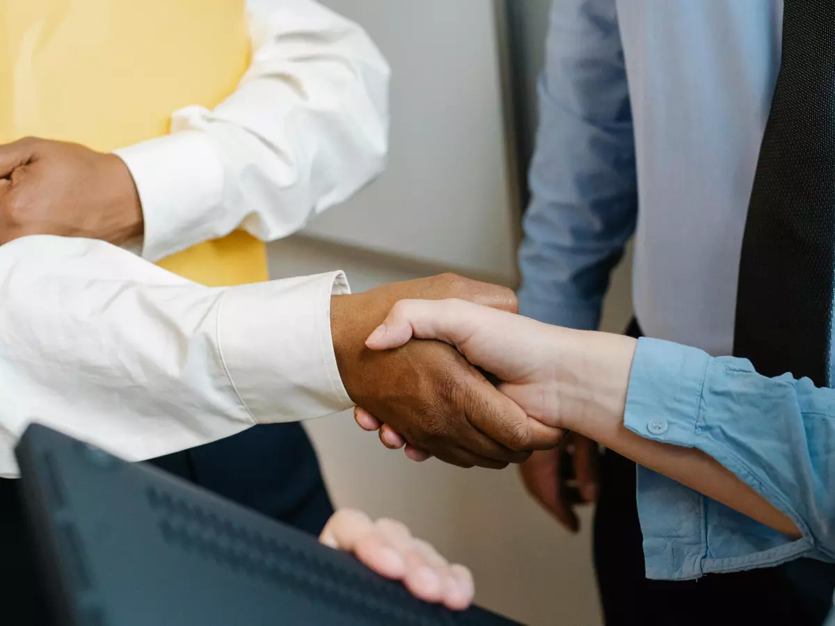 Two businessmen shaking hands in a meeting, a third person is observing them.