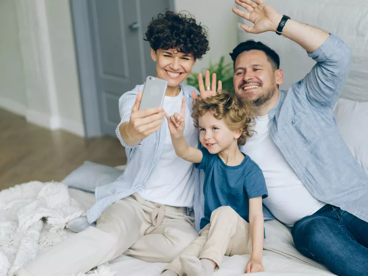 A family of three is taking a selfie on a bed.