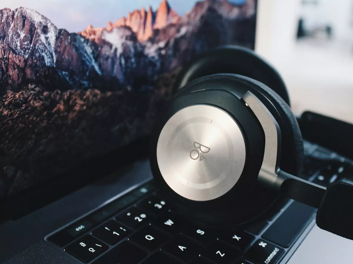 A close-up shot of a pair of Bang & Olufsen Beoplay H100 headphones resting on a laptop keyboard. The headphones are black with a silver trim and the Bang & Olufsen logo is visible on the earcup.