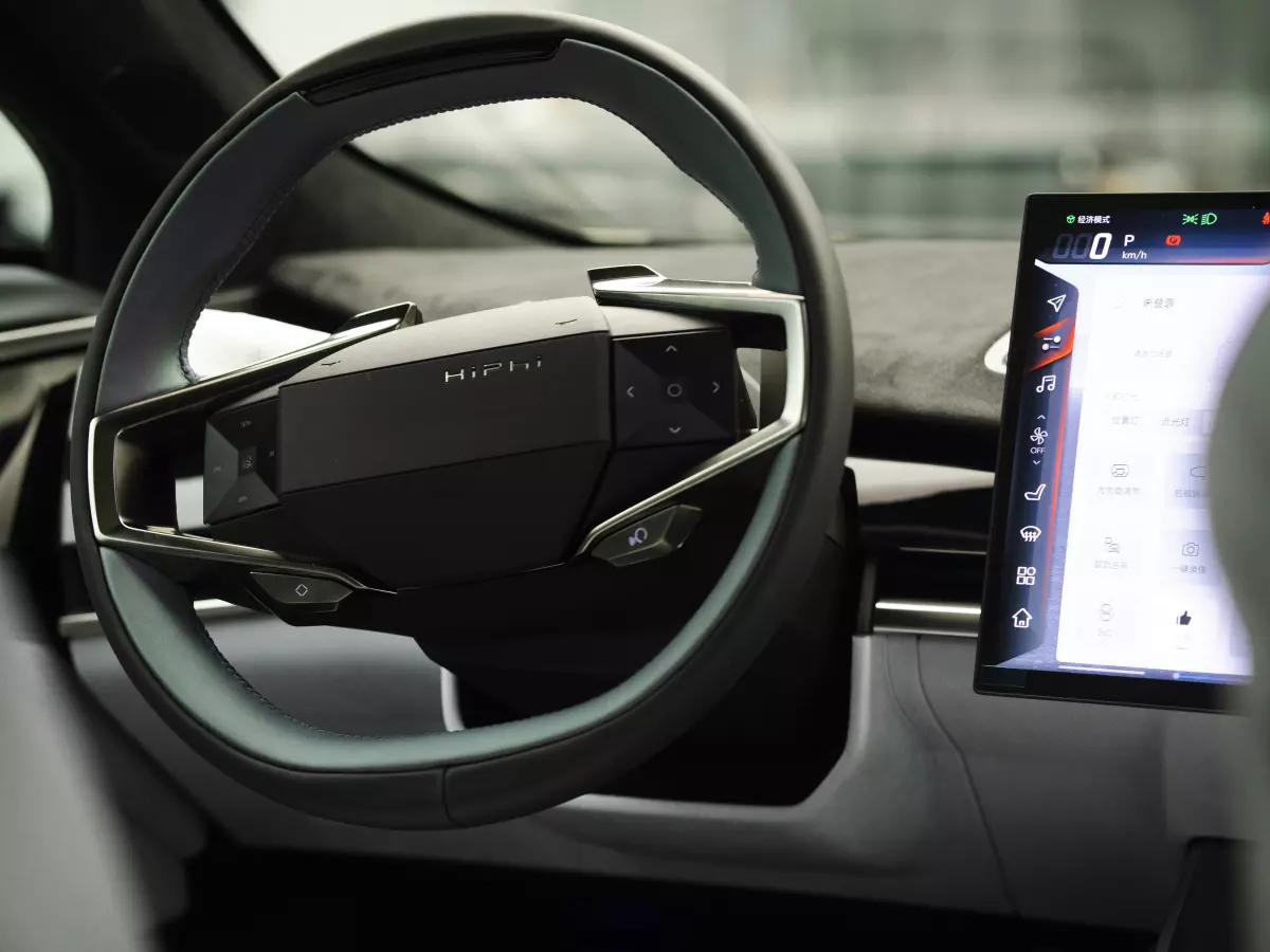 The interior of a modern electric car, showcasing a futuristic steering wheel and a large touchscreen display, likely displaying battery management information and software features.