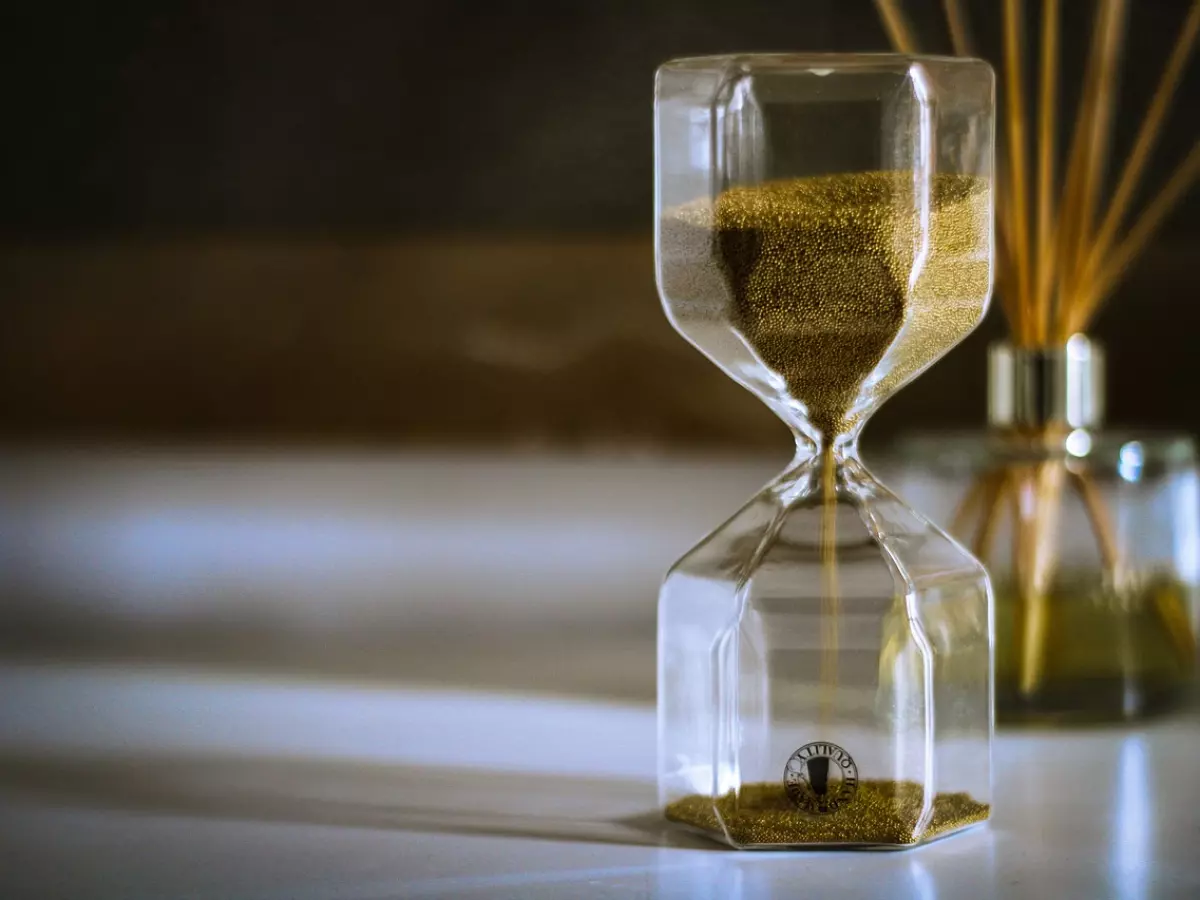 A golden hourglass in the foreground with a diffuser bottle in the background.