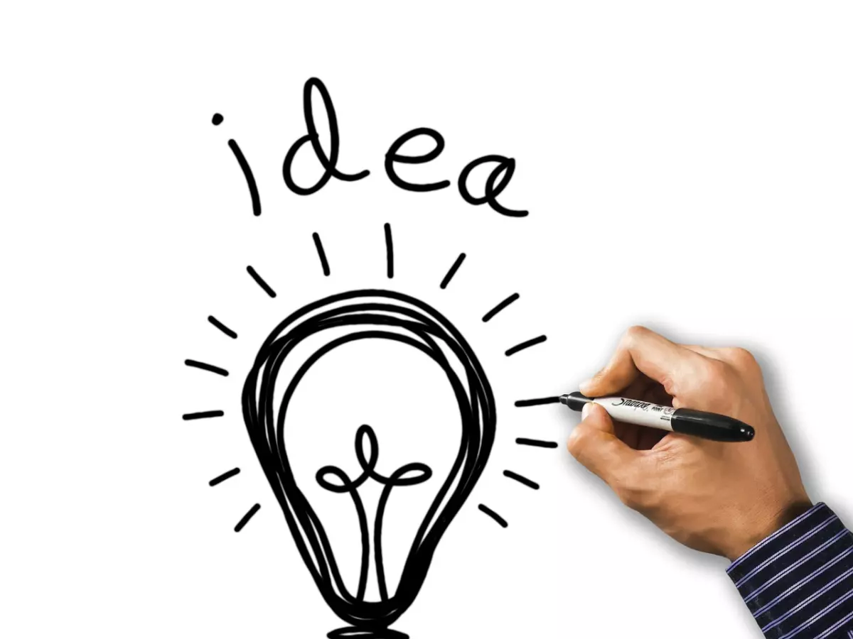 A hand drawing a lightbulb on a white board, representing ideas and innovation.