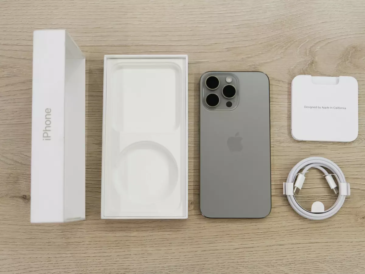 A picture of an iPhone 15 Pro with its accessories, including the box, charging cable, and wireless charger.