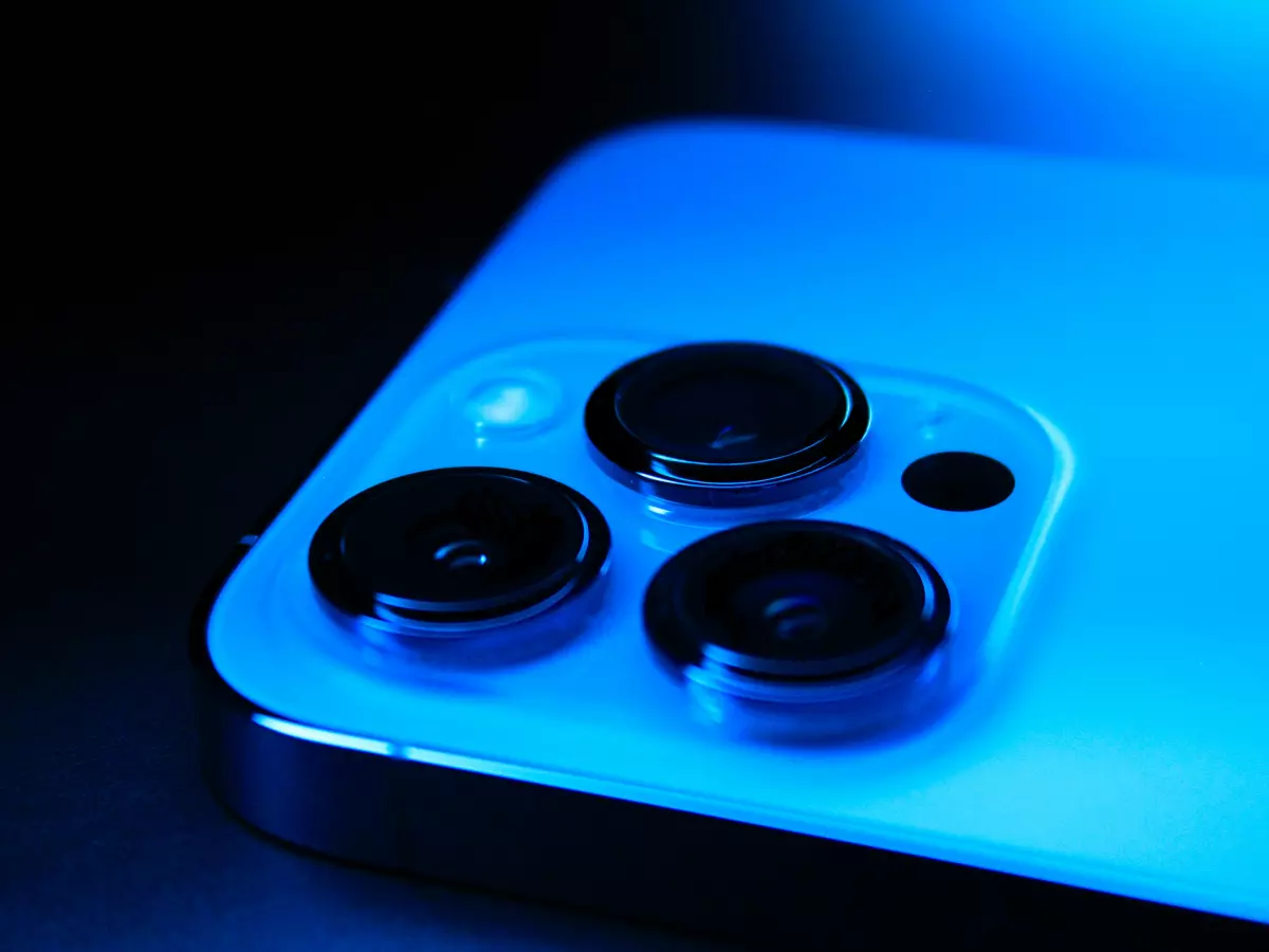 Close-up of a smartphone's triple-lens camera system, illuminated by blue light against a dark background.