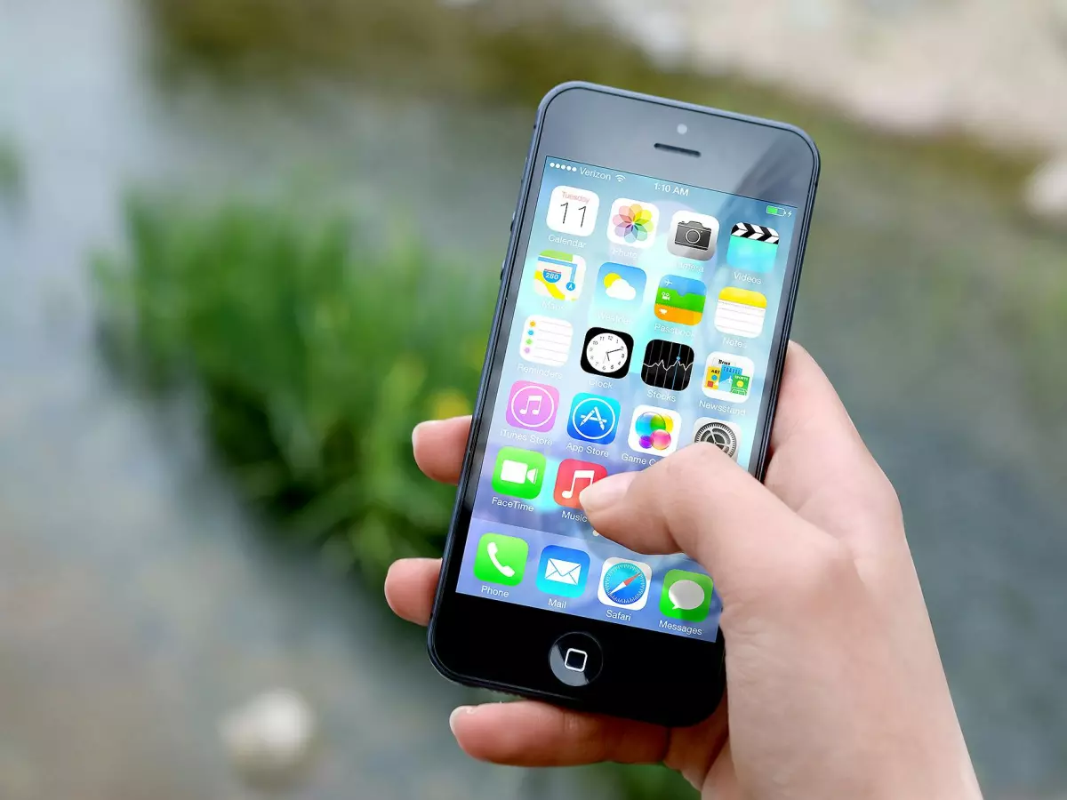 A hand holding a smartphone, with a close-up of the screen showing icons