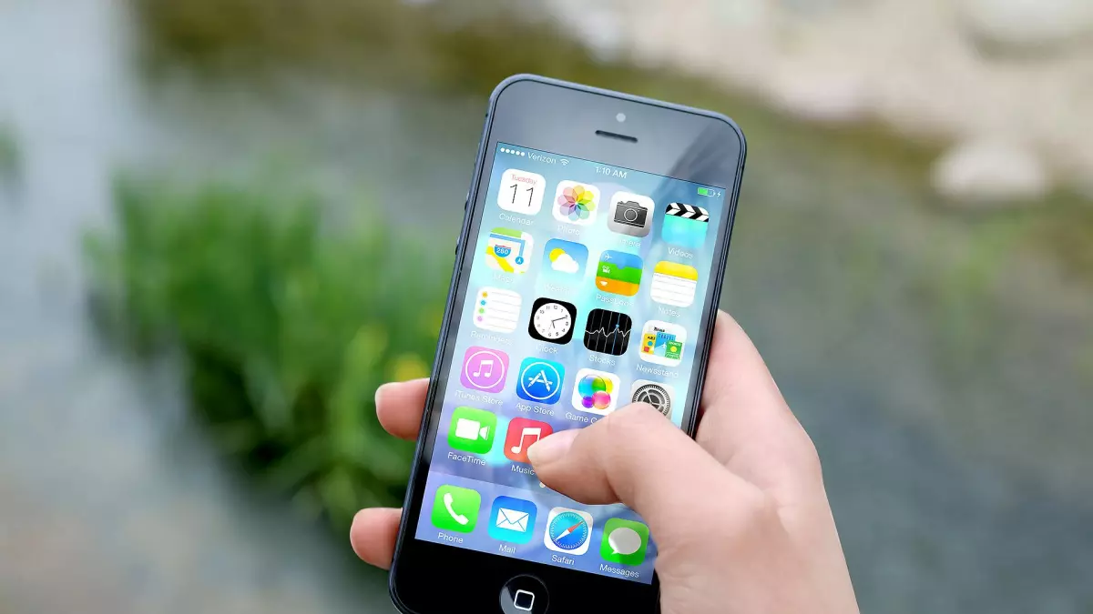 A hand holding a smartphone, with a close-up of the screen showing icons