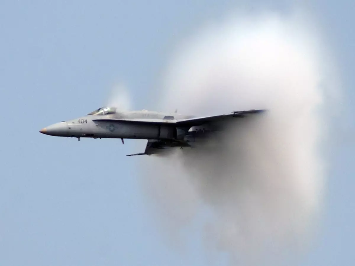 A fighter jet breaking the sound barrier, creating a large cloud of condensation.