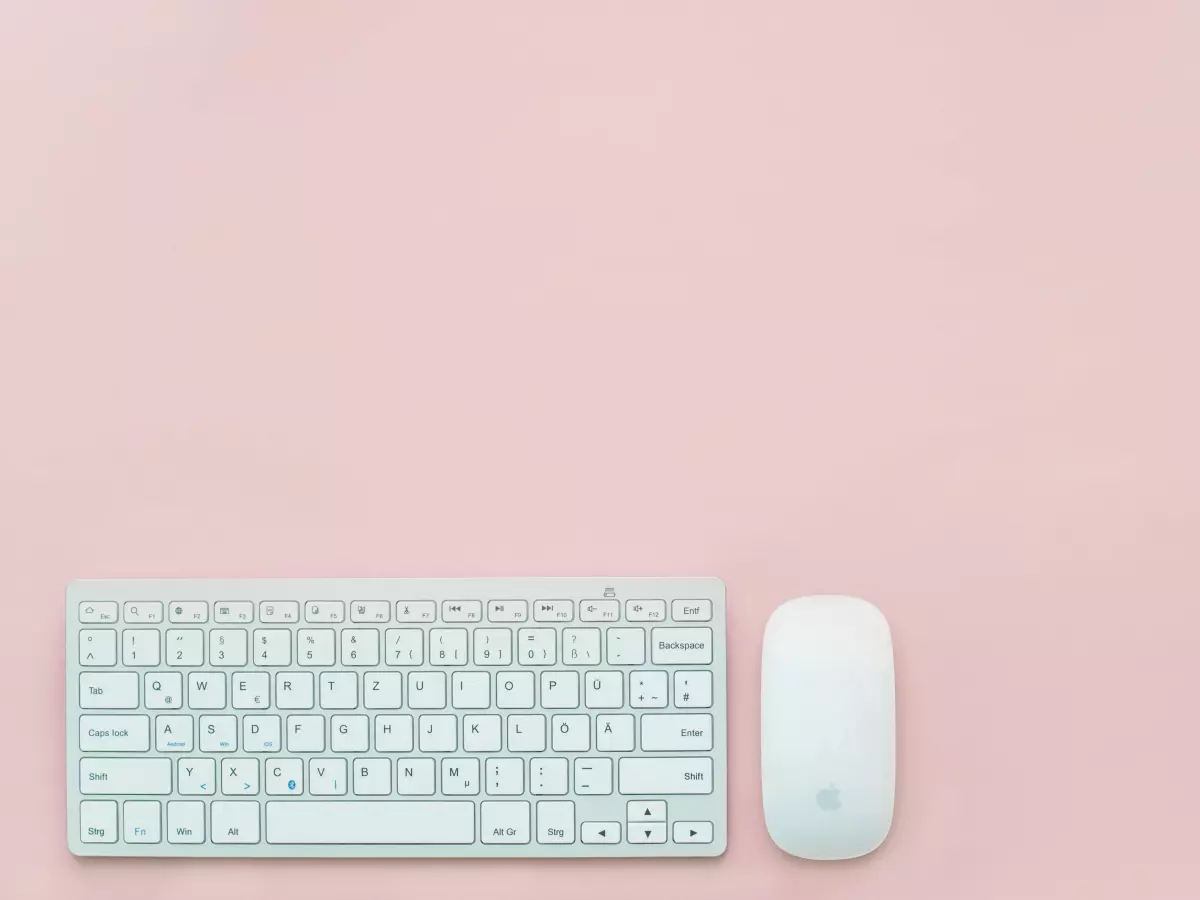 An Apple iMac, white with a black screen, on a white table with a white keyboard and mouse.