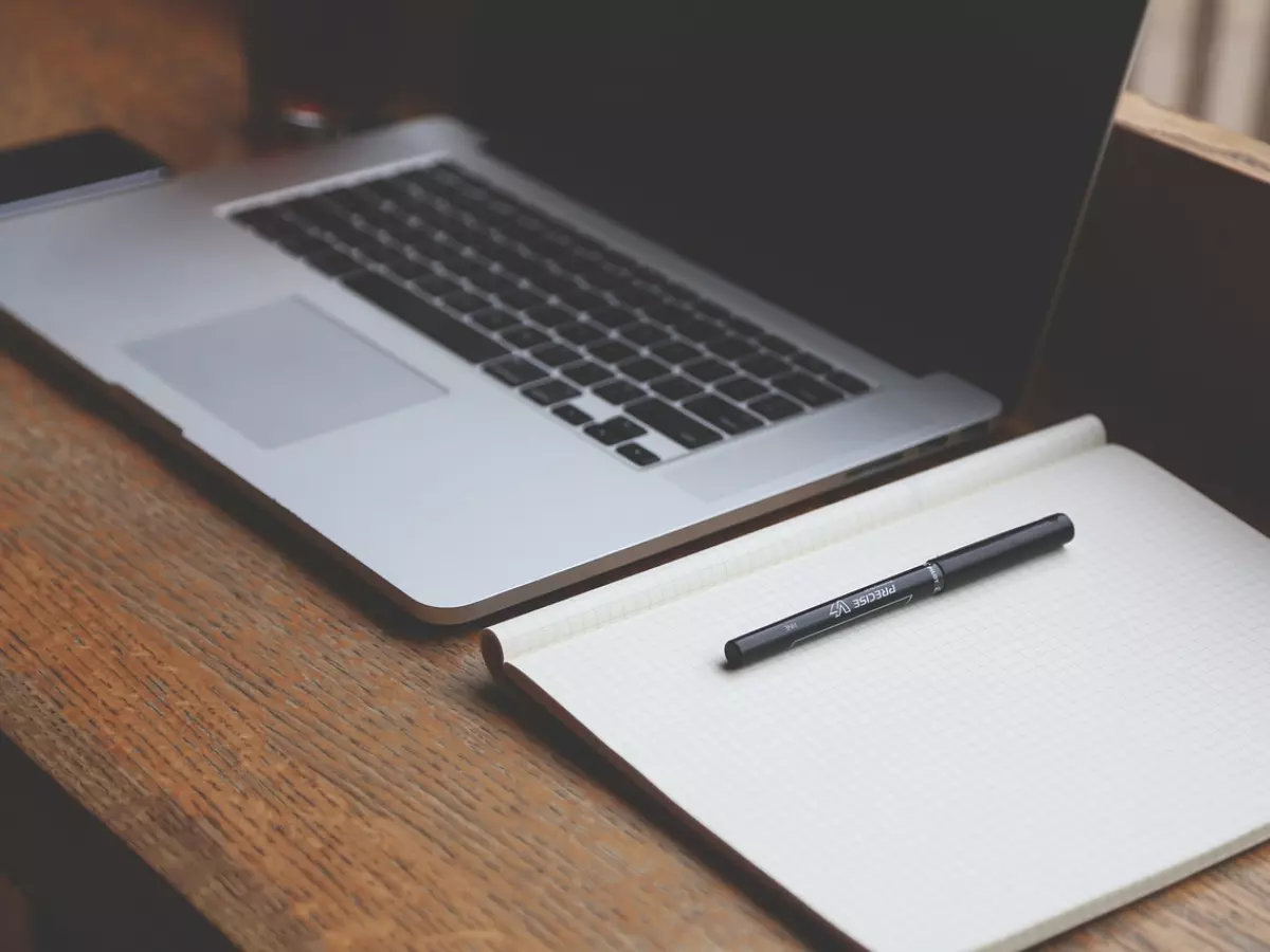 A laptop and a notebook on a wooden table.