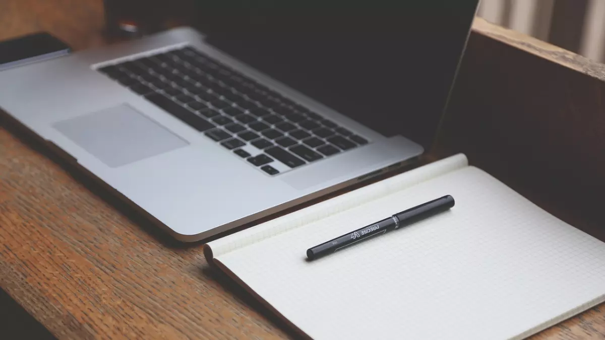 A laptop and a notebook on a wooden table.