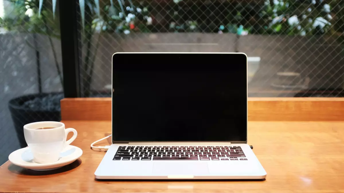 A laptop sits on a wooden table next to a cup of coffee.