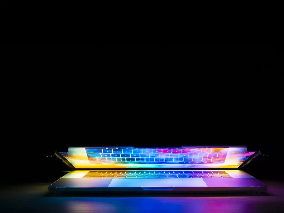 A laptop with a colorful galaxy screen, lit up in a dark room.