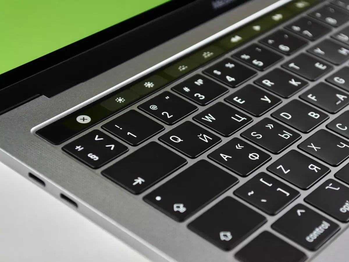 A close-up shot of a silver laptop with USB-C ports on the left side of the computer. The keyboard is visible with white backlit keys.